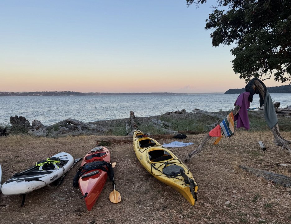 Kayaks and a paddleboard drawn up on the beach at Blake Island at dusk