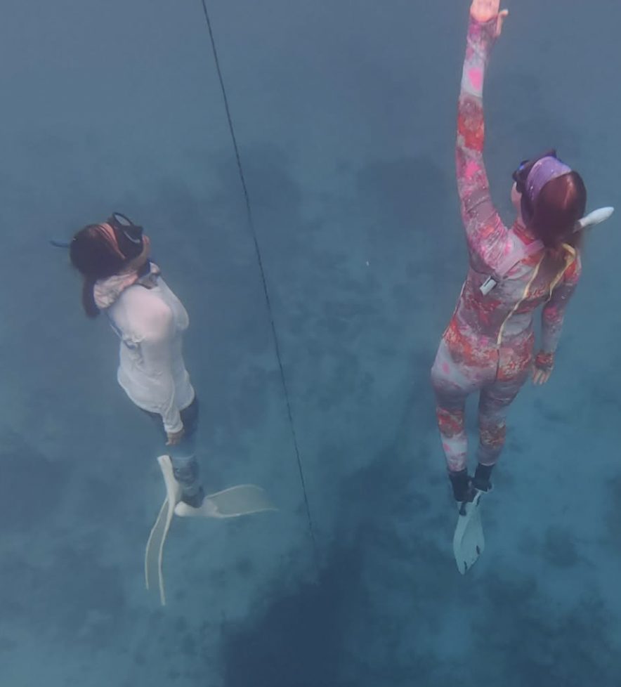 Two free-divers rising along a line through blue water