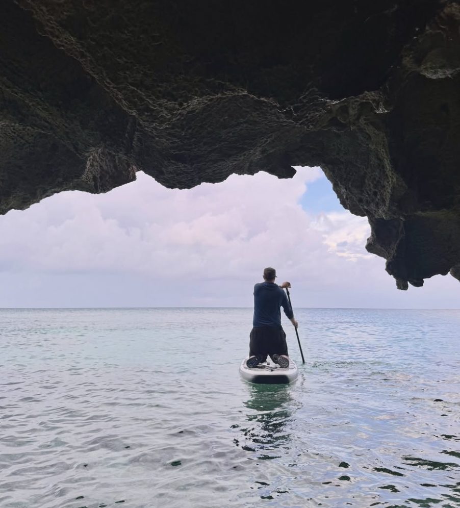 Paddle-boarding out of a sea cave, its rock ceiling overhead and flat water beyond
