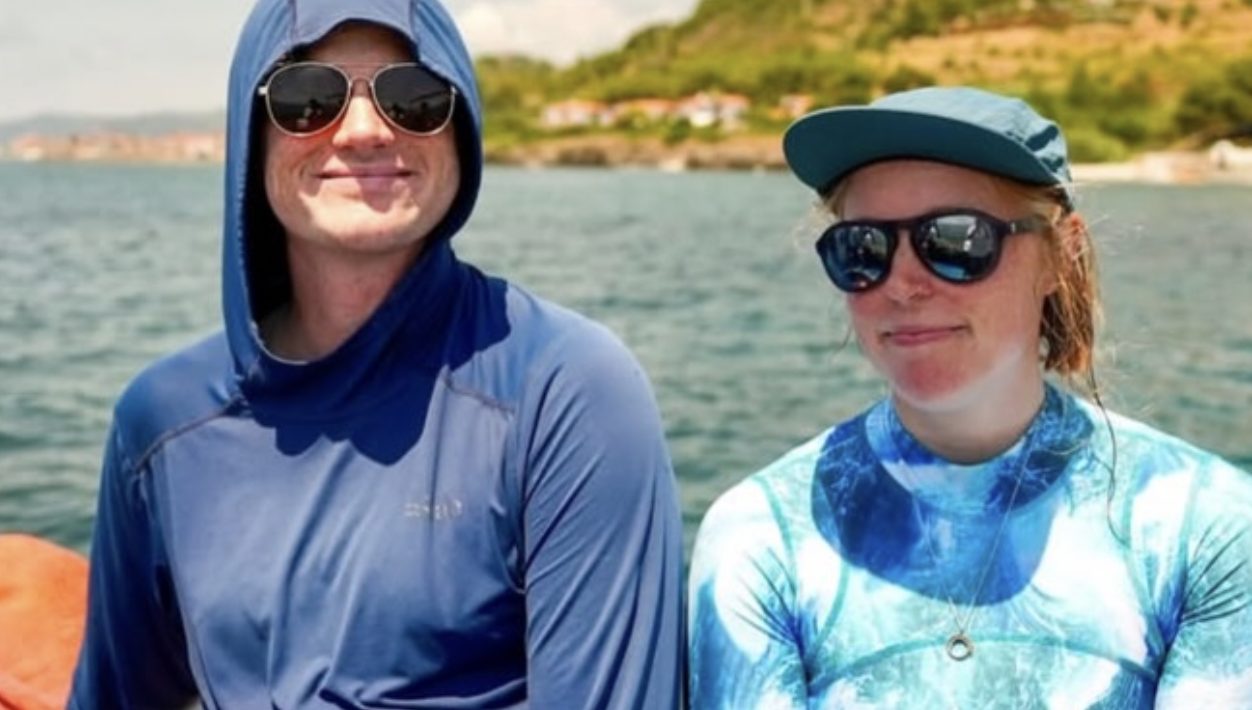 Sean and Kate on a boat off the Cilento coast, hoods and caps on, the shore behind